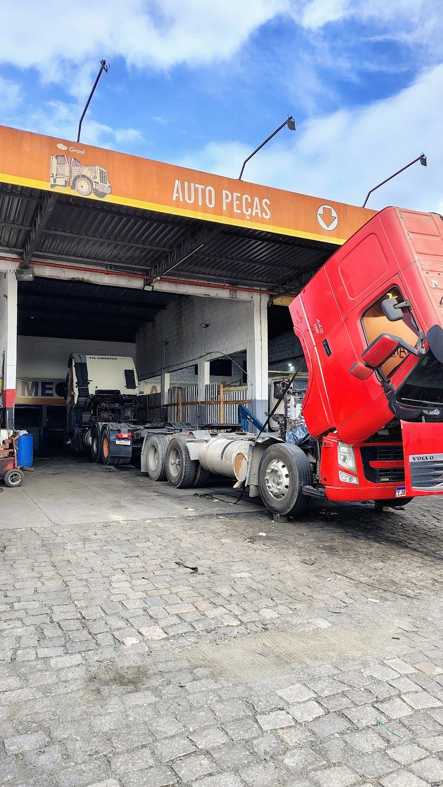 Caminhão de cabine vermelha em manutenção na oficina Ferrugem.